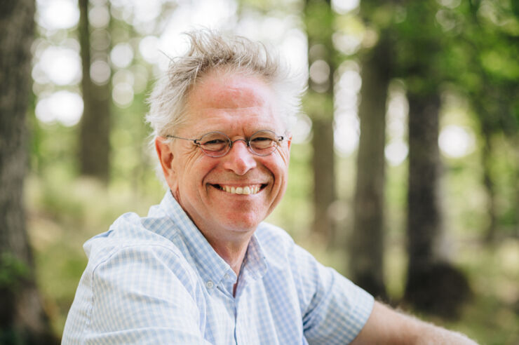 Portrait picture of Björn-Ola Linnér sitting outside with some trees in the background.