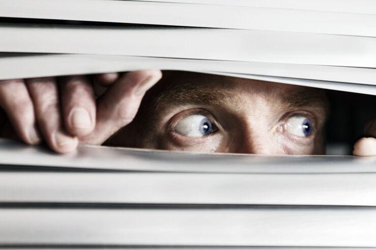 Man looking sideways through venetian blind.