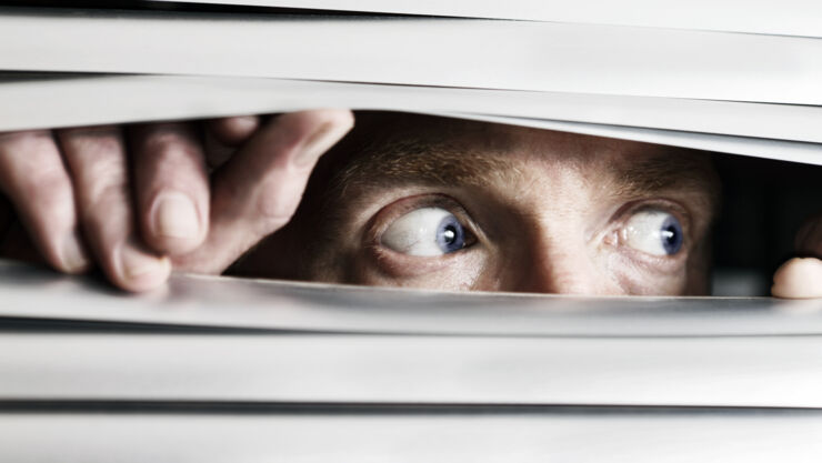 Man looking sideways through venetian blind.