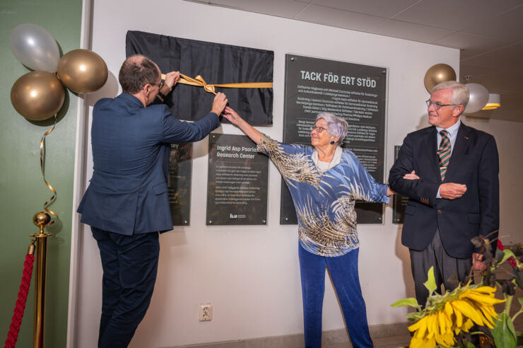 A man and a woman uncover a plaque, another man watches.