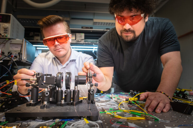 Två personer i ett labb med ett laserinstrument som står på ett bord fullt med sladdar.