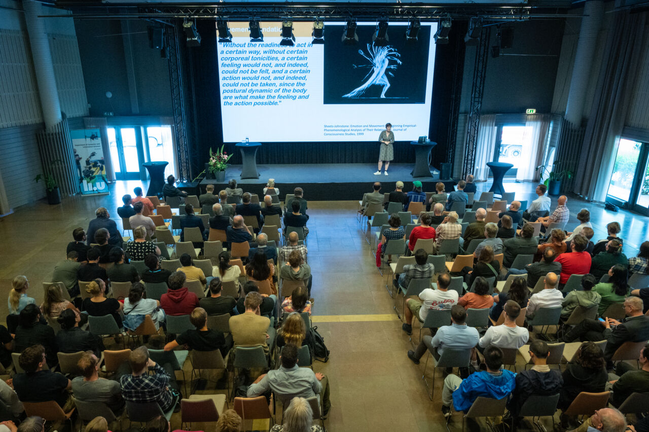Fullsatt konferenssal med talare på scen
