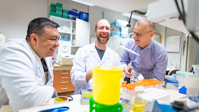 Tre män skrattar medan de arbetar i ett laboratorium.