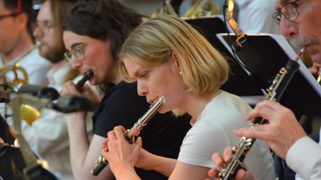 The wind section in an orchestra where the focus is on a woman playing the flute.