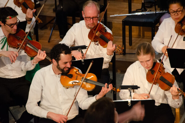 Delar av stråksektionen i en orkester med fem personer som spelar violin.