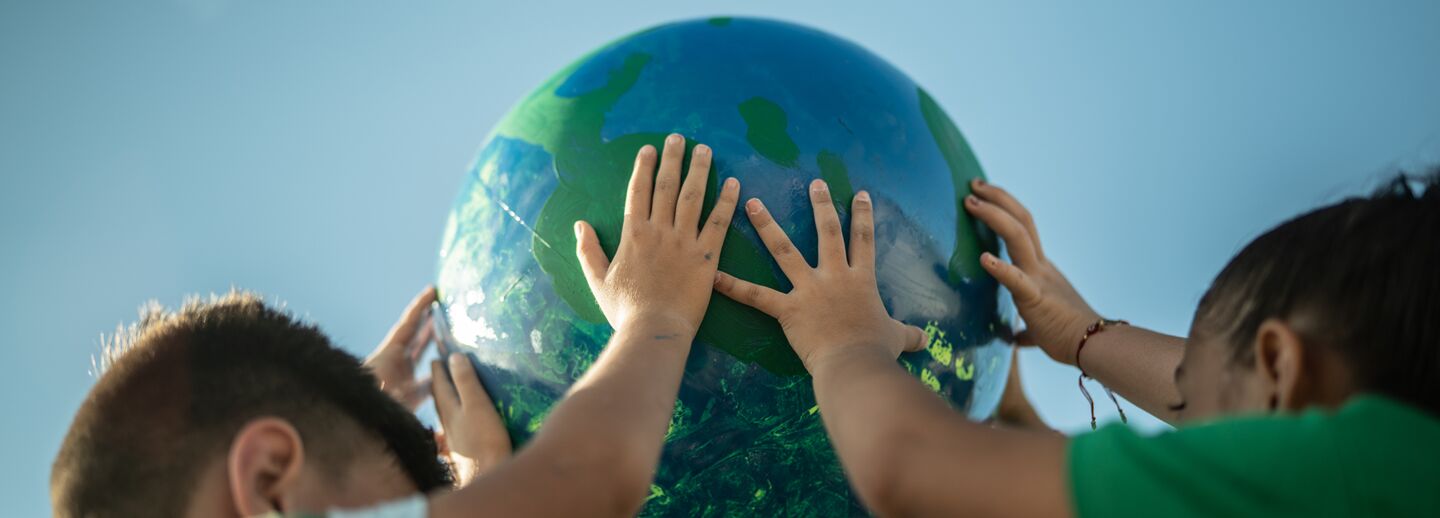 Barn som håller en jordglob ovanför sina huvuden.