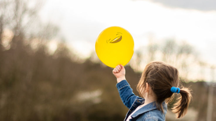 Barn som håller en gul ballong med smiley