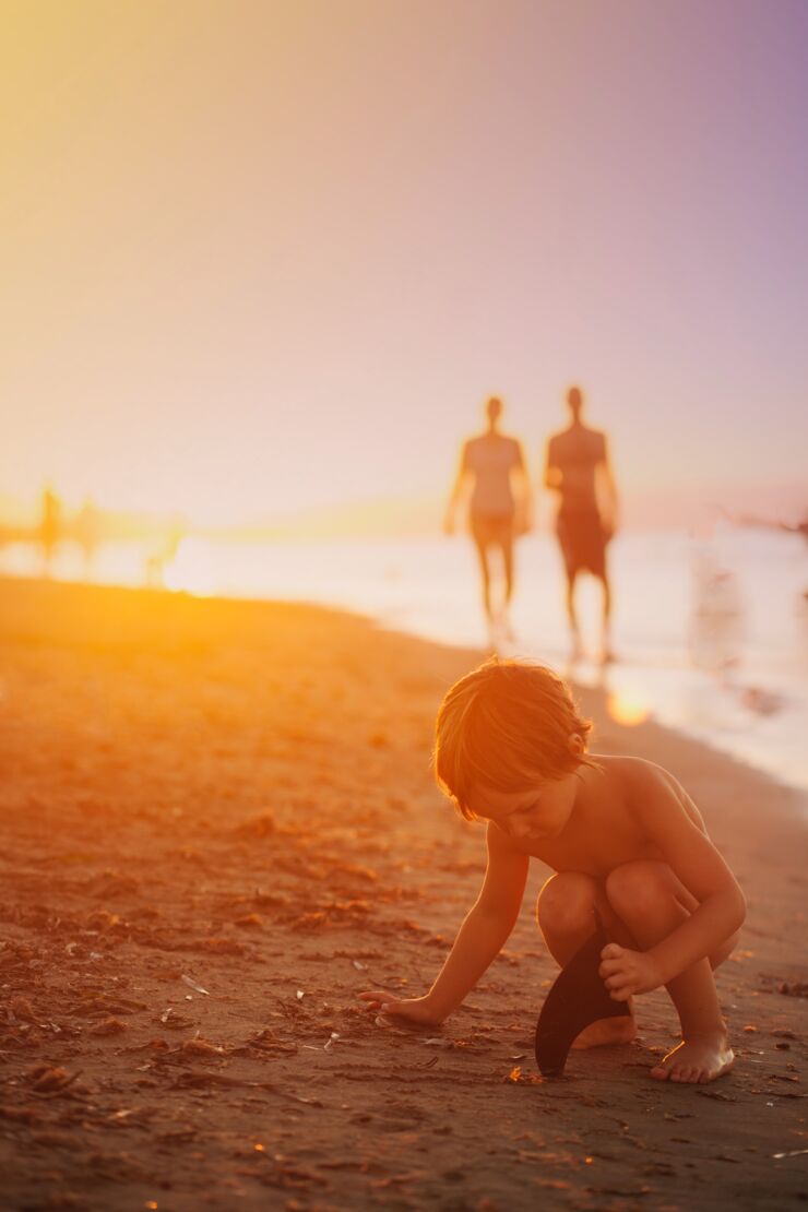 Ett barn på en strand med två vuxna personer i bakgrunden.