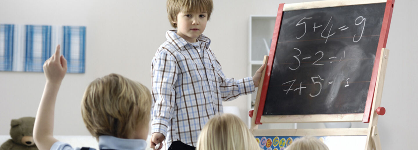 A boy standing next to a black board. 