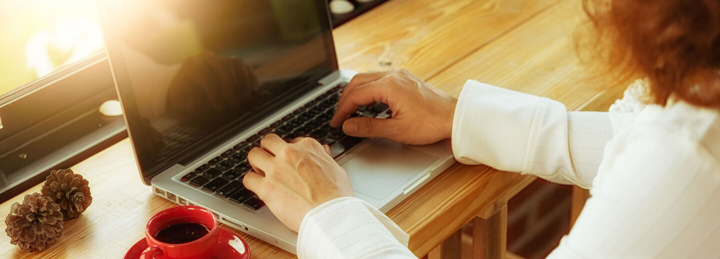 A close-up of a woman's hands typing on a laptop computer.