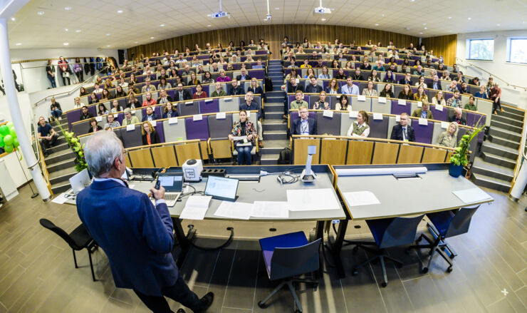  A person lectures to a large hall of people listening.