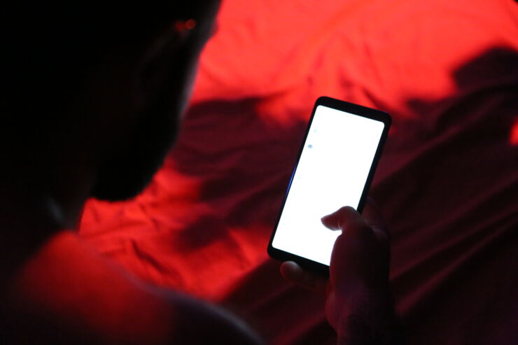 A person is holding a mobile phone that is lit up in a dark room with red lights