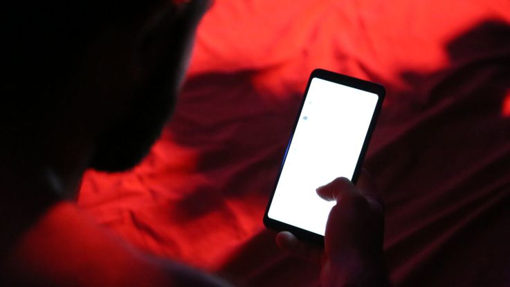 A person is holding a mobile phone that is lit up in a dark room with red lights