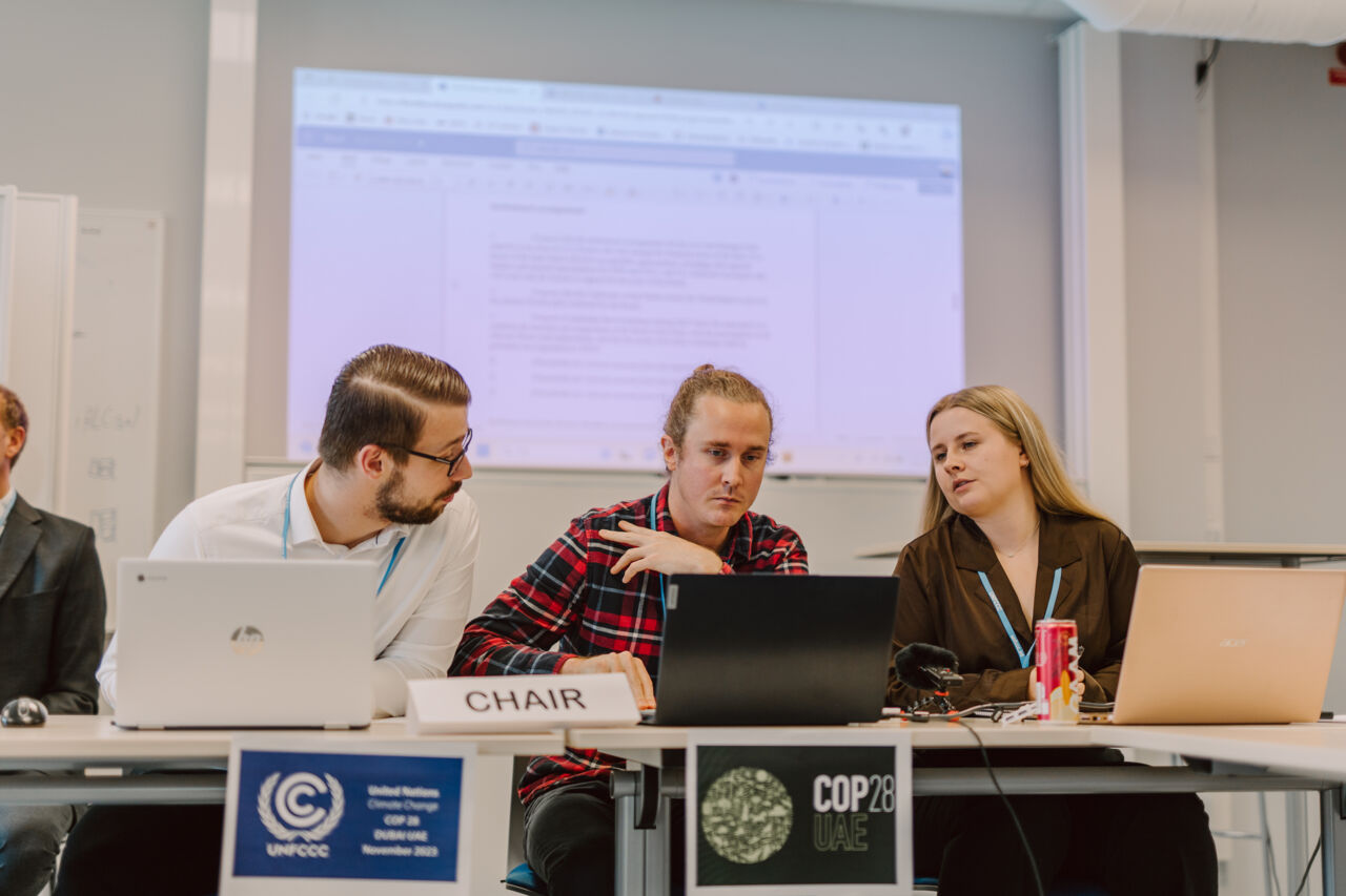 Tre studenter sitter på rad vid en skylt med texten 