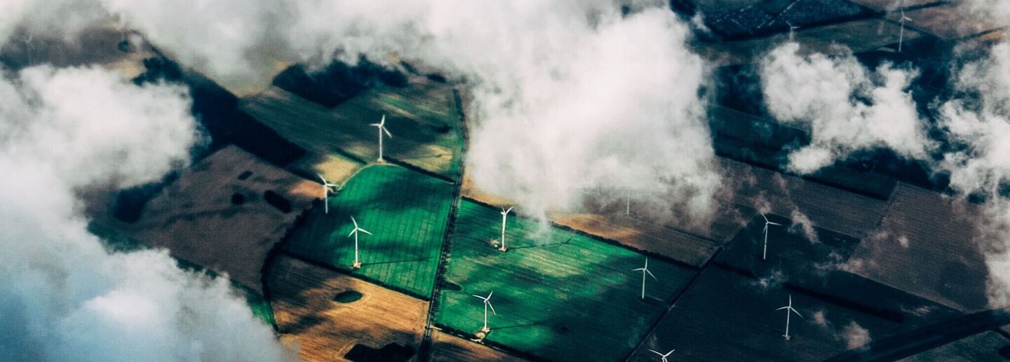 Wind turbines on green fields seen behind the clouds from high above