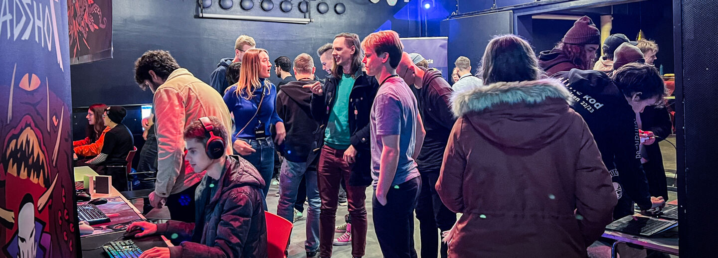 Ett rum med personer som spelar dataspel och personer som ser på då de gör det.