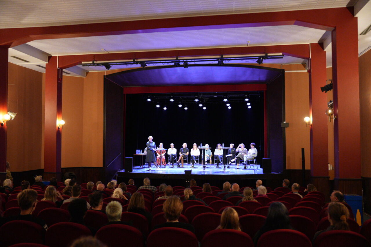 Personer på en upplyst scen och publik i förgrunden