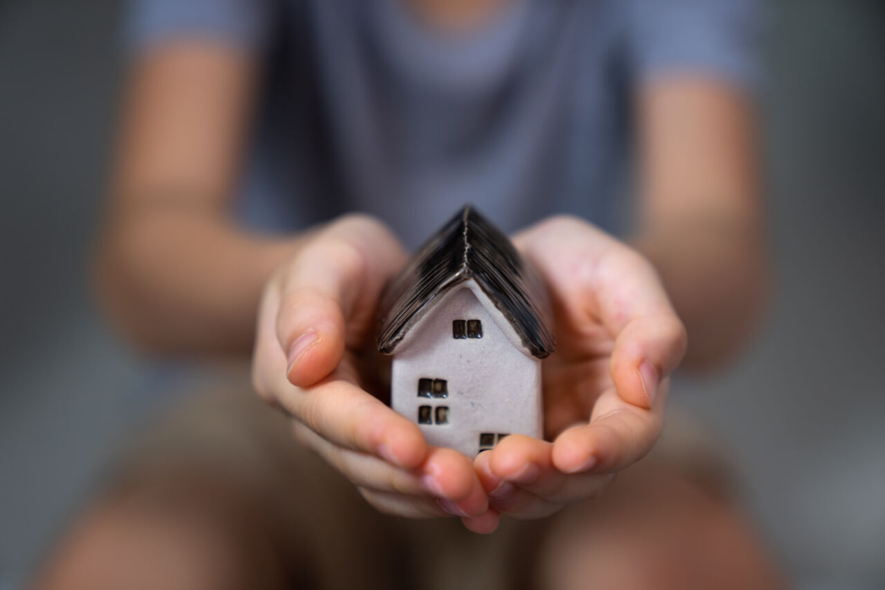 Two hands holding a small ceramic cottage 