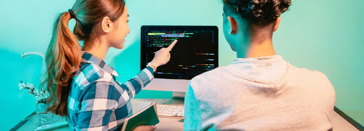 Students discussing programming code at a computer screen
