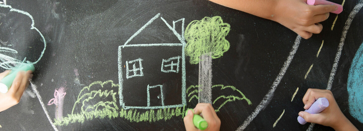 Barnhänder målar ett hus med kritor