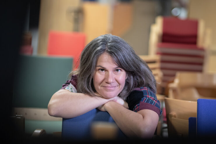 Marianna Lena Kambanou sits leaning forward over the back of a blue chair, with her arms crossed. 