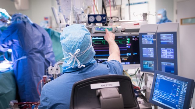 En person i operationskläder pekar på en skärm i en operationssal.