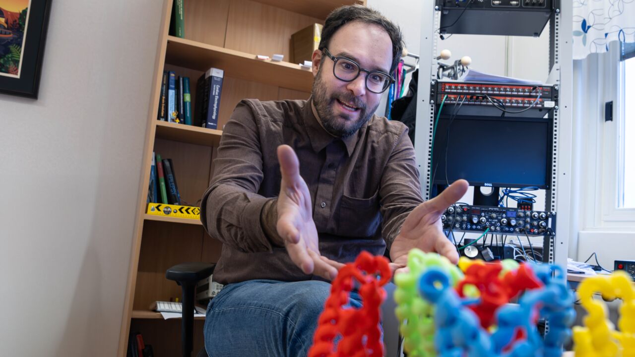 Researcher Antonios Pantazis sits in his office and shows his 3D model of ion channels in different colors.