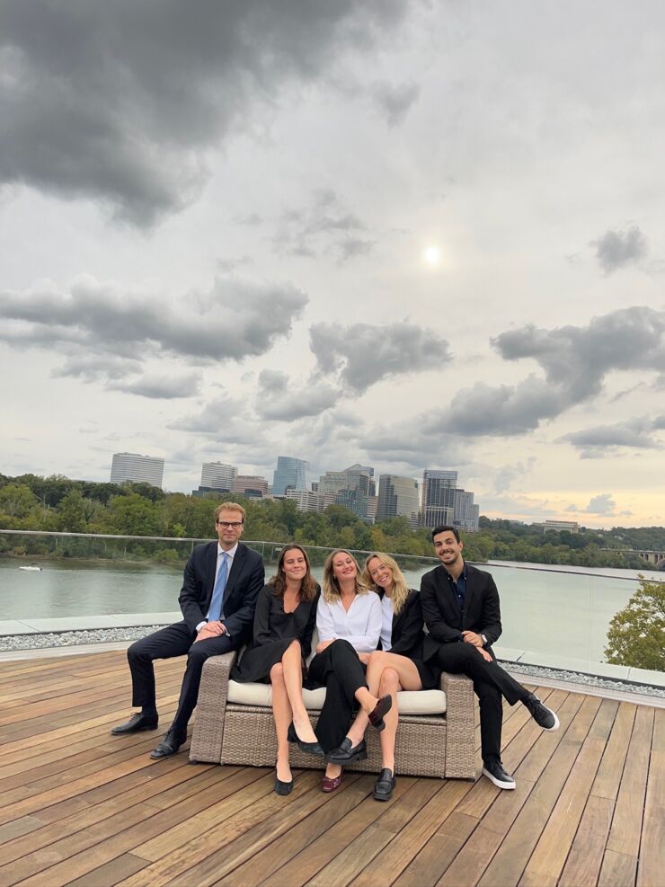 Five people sit on a terrace with tall buildings in the background