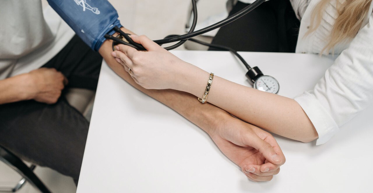 Närbild av armar på ett bord, en läkare tar blodtryck på en patient.