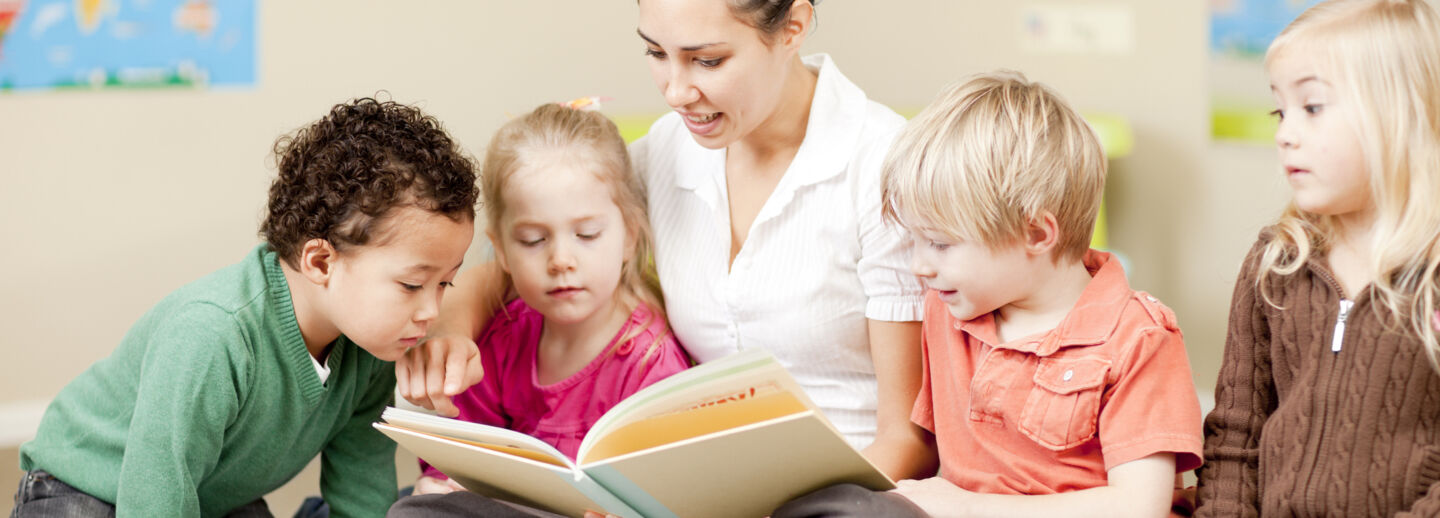 A female teacher reading a book to a group of a children.