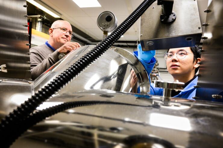 Two persons behind large lab equipment.