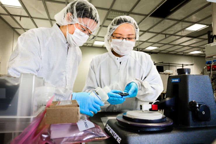 Två personer i labbrockar och ansiktsmaski i ett labb.