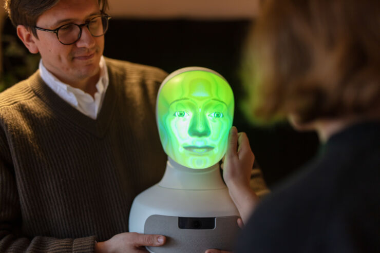 Two persons holding a robot head that lights up green