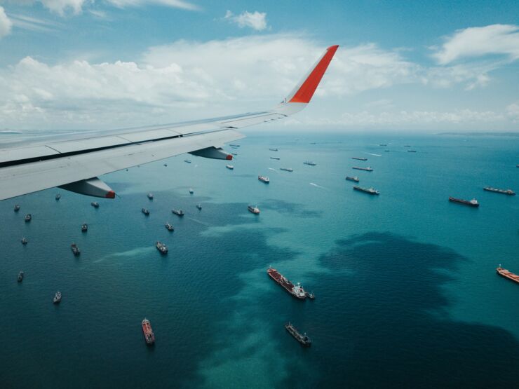 View of an airplane wing in the air with ships on the sea below.