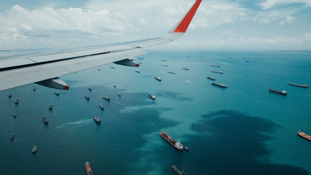 View of an airplane wing in the air with ships on the sea below.