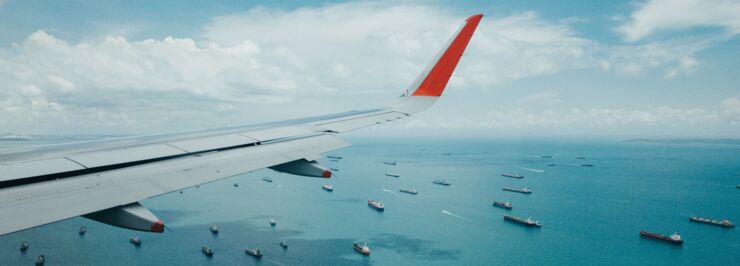 View of an airplane wing in the air with ships on the sea below.