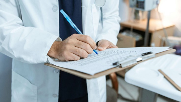 En läkare fyller i ett dokument med en penna i ett rum på ett sjukhus.