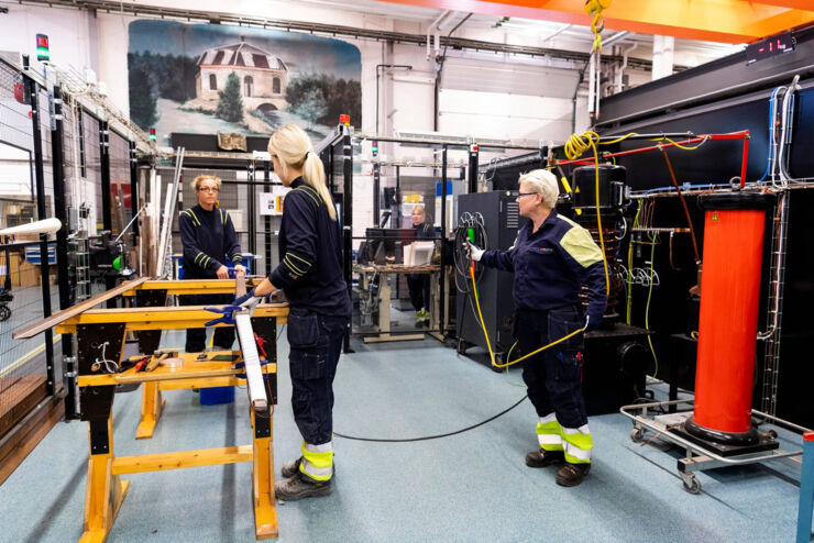 Tre kvinnor i blåa arbetsoveraller som jobbar på ett fabriksgolv