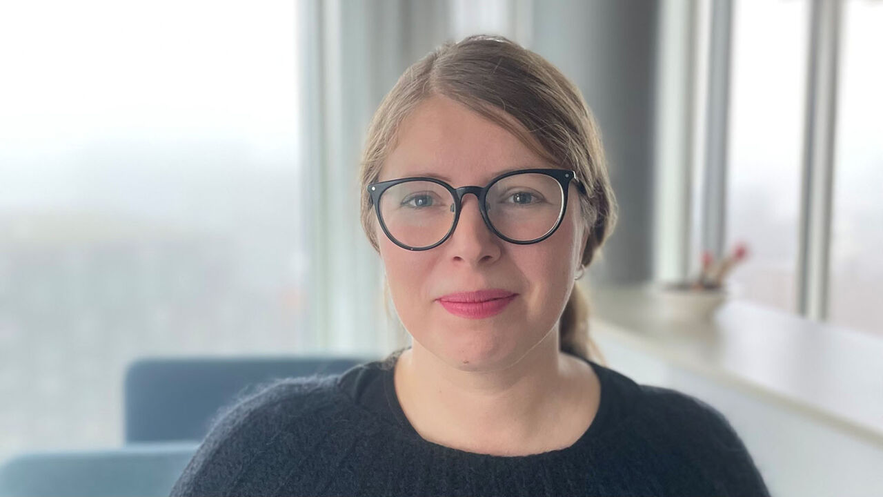 Porträttbild på en kvinna med mellanblont uppsatt hår, svarta glasögon och rött läppstift.