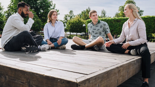 4 studenter sitter utomhus på marken med benen i kors på 