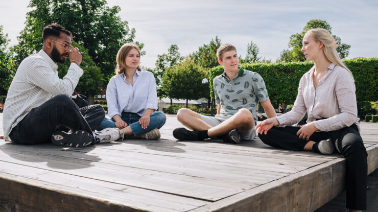 4 studenter sitter utomhus på marken med benen i kors på 