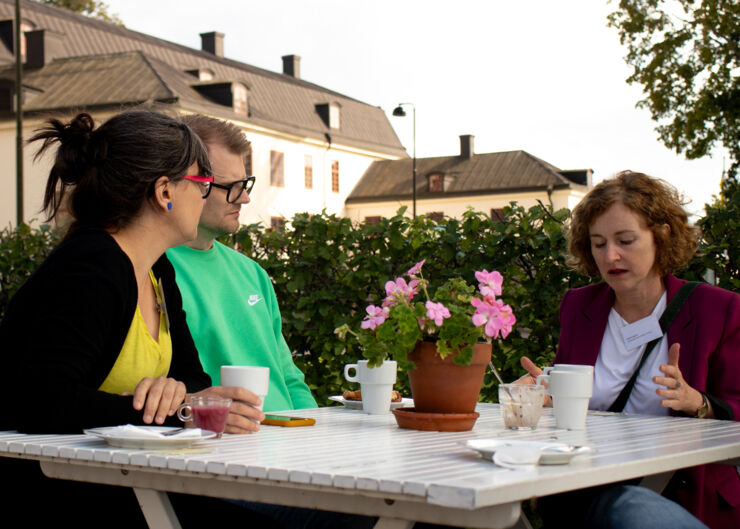 Tre personer sitter vid ett bord utomhus och diskuterar