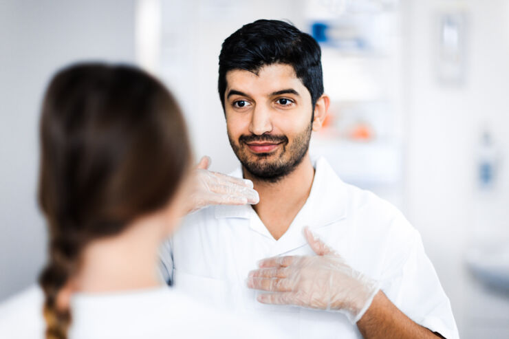 Person i sjukhusskjorta och plasthandskar kommunicerar med patient, som har ryggen mot kameran.