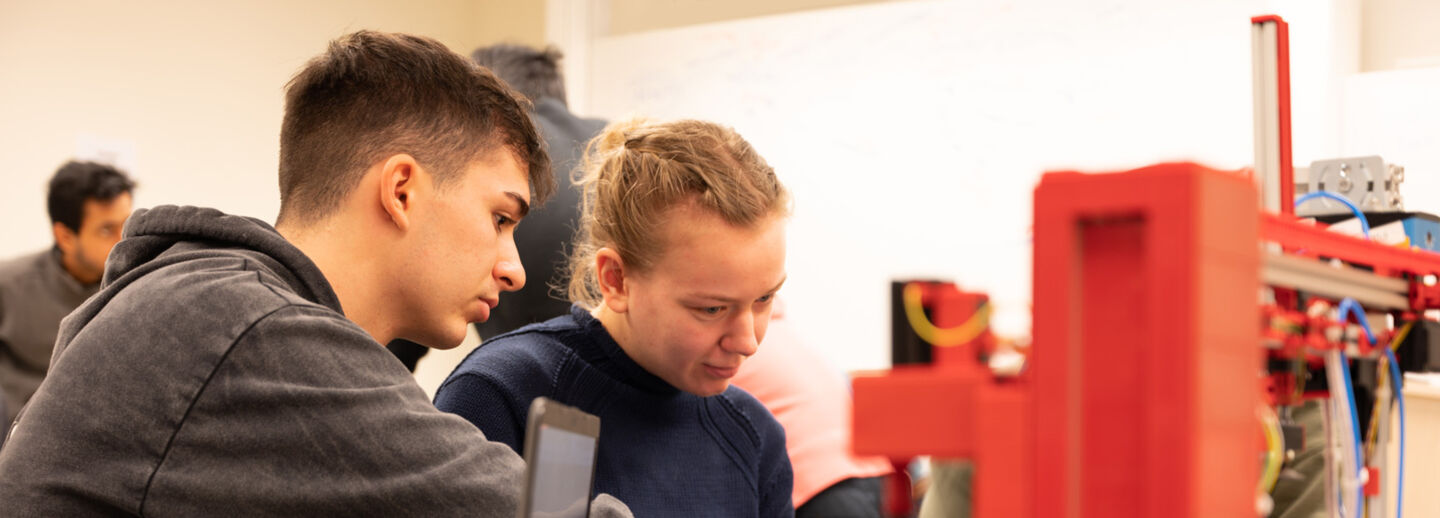 Två studenter arbetar med en röd maskin i labb