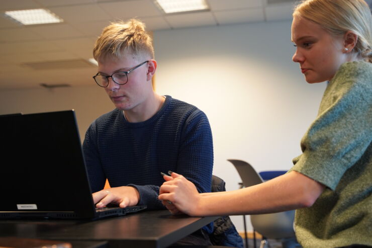 Två elever sitter vid skrivbord och tittar i datorn. 