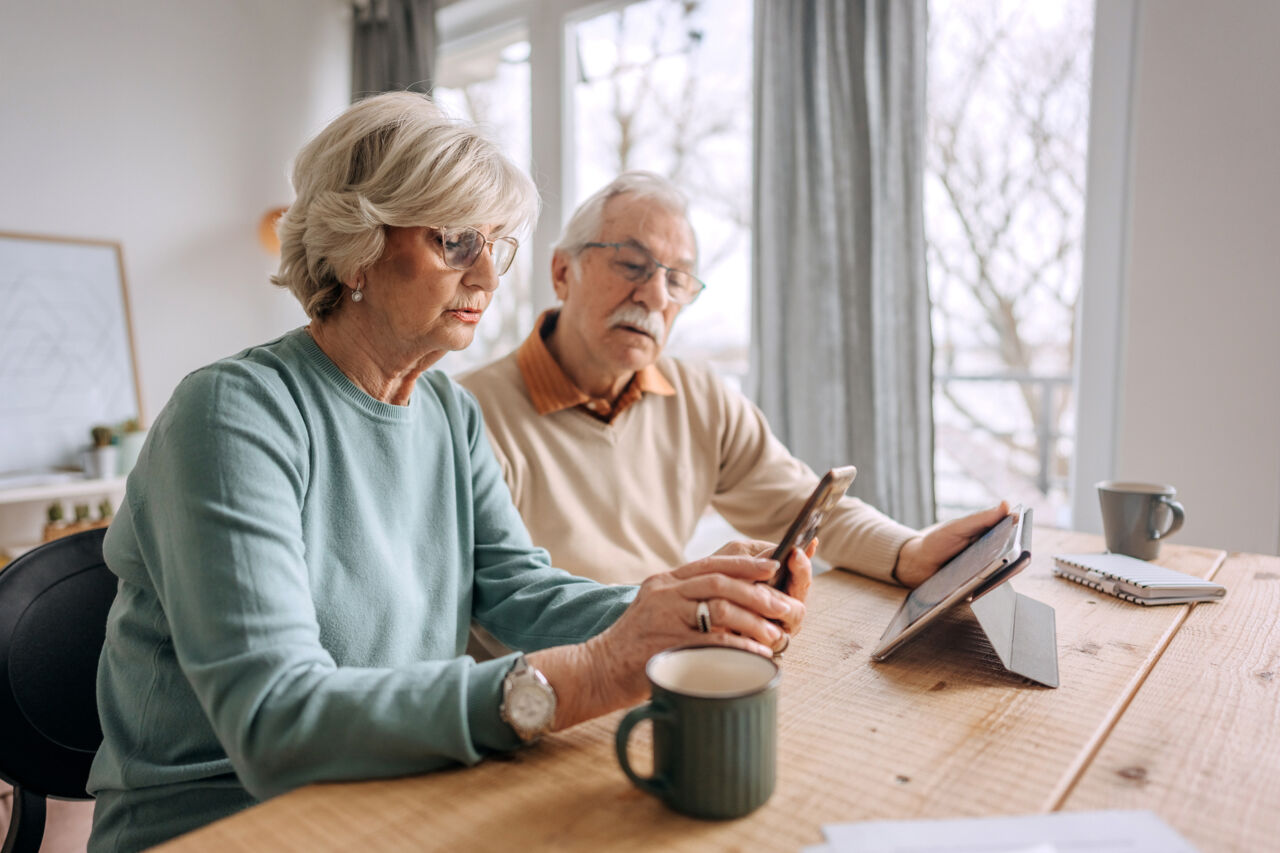 An elderly couple sitting at a table looking at a mobile phone.