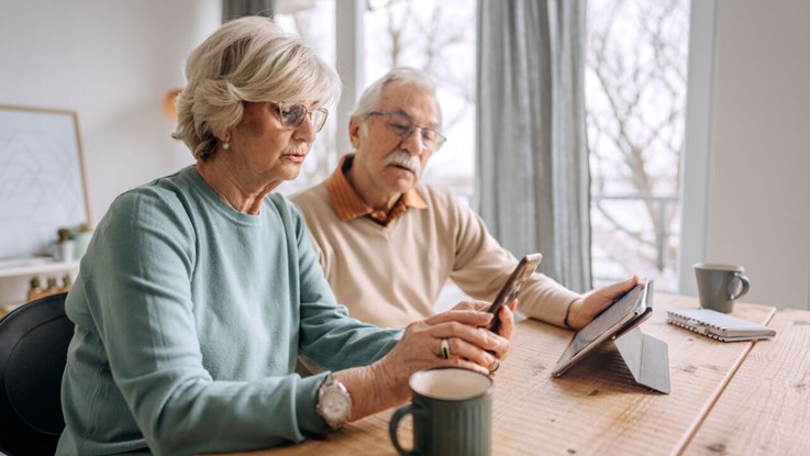 Äldre par sitter vid ett bord och tittar på en mobiltelefon.
