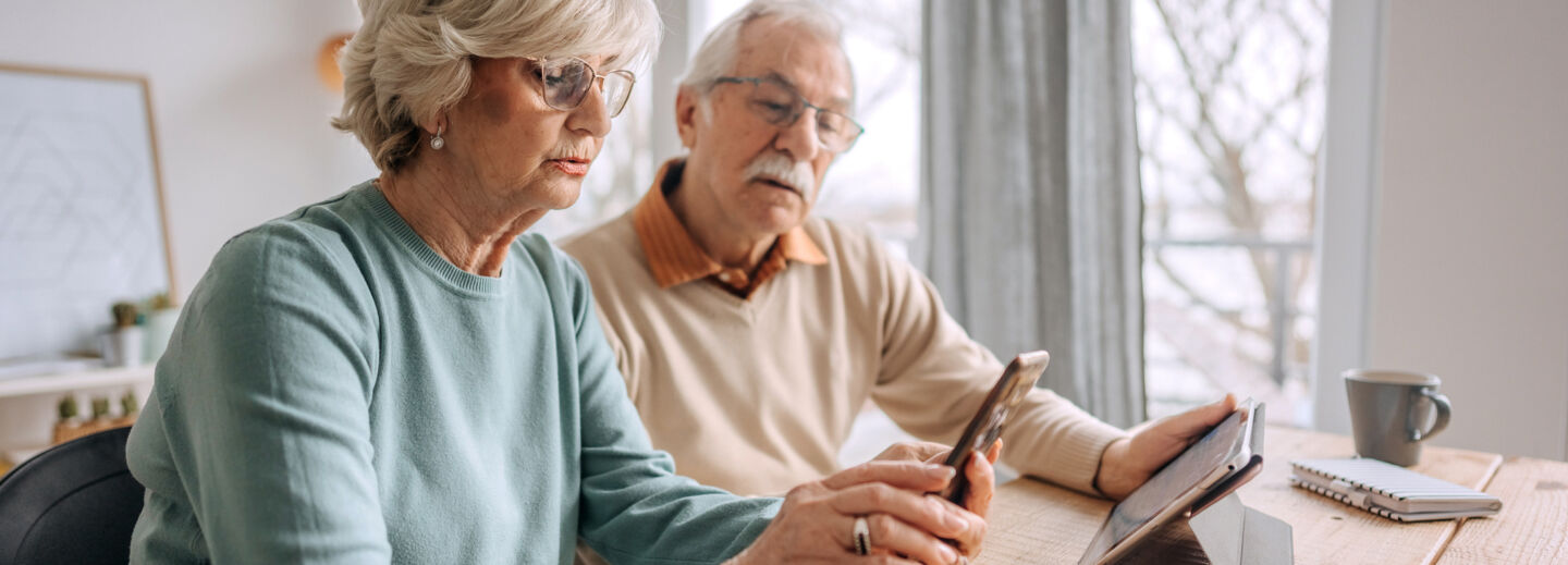 An elderly couple sitting at a table looking at a mobile phone.