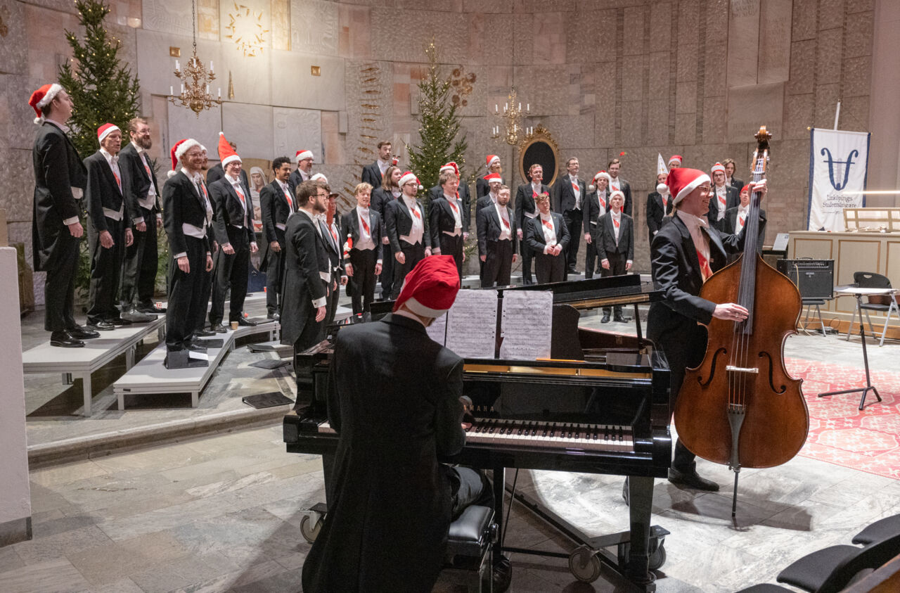 Male choir in evening dress and santa's hats sings and plays.