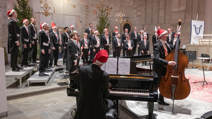 Male choir in evening dress and santa's hats sings and plays.